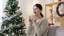 Portrait Pretty Lady In Winter Casual Wear Sitting By Christmas Tree On The Sofa Is Heaving A Sigh Of Relief After Sipping Her Hot Drink.
