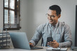 © kamiphotos - Businessman is sitting and working in the office, Employee is looking for information on laptop, An entrepreneur is talking on the phone with a company customer, startup.