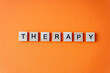 © Real_life - Word therapy. The phrase is laid out in wooden letters top view. Orange flat lay background. Destressing hobby concept