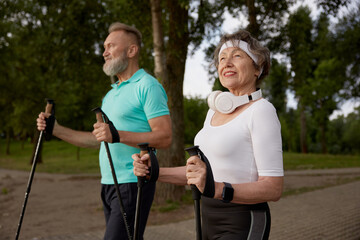 Wall Mural - Elderly woman and man married couple enjoying nordic walking in city park