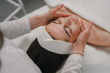 Wall Mural - Beautician's hands applying facial cleansing foam on woman's face massaging skin in cosmetology clinic. Cosmetologist making skincare procedure in beauty salon.