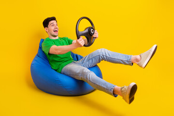 Canvas Print - Full size photo of ecstatic guy wear t-shirt sit on bean bag look empty space hold steering wheel isolated on yellow color background