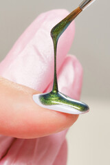 Wall Mural - Close up process of applying green glitter varnish. Woman in salon receiving manicure by nail beautician. Green nail polish drop and brush, macro. Shallow depth of field