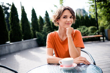 Canvas Print - Photo of cheerful pretty girl dressed orange t-shirt sitting cafe enjoying morning coffee outdoors urban town park