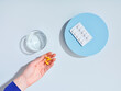 Flat lay creative composition with food supplement pills, glass of water and female hand on colorful background