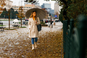 Wall Mural - Young woman with umbrella walking down a city street covered with leaves on a autumn rainy day