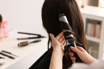 Wall Mural - Hairdresser working with client using curling hair iron in salon, closeup