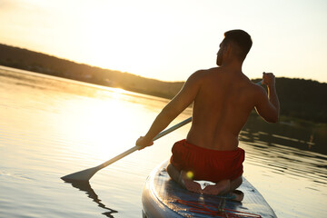 Wall Mural - Man paddle boarding on SUP board in river at sunset, back view