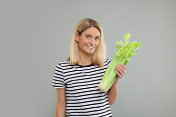 Wall Mural - Woman holding fresh green celery bunch on light grey background