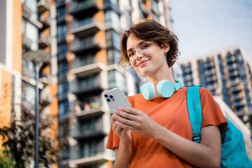 Poster - Photo of charming cute lady wear orange t-shirt spectacles rucksack typing message modern device outside urban city street