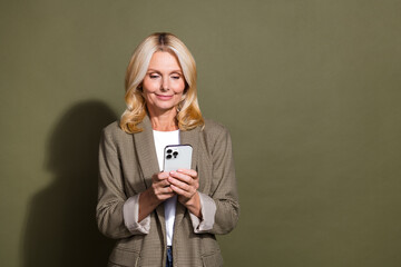 Canvas Print - Photo of senior businesswoman influencer surf social networks using smartphone wear formal jacket isolated on khaki color background