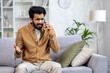 © Liubomir - Angry angry man talking on the phone at home, dissatisfied customer sitting on the sofa in the living room yelling at the interlocutor.