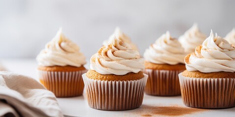 Wall Mural - Pumpkin cupcakes on a white table topped with cream cheese frosting and dusted with cinnamon