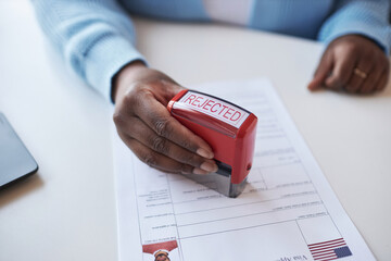 Hand of young African American female worker of visa application center stamping document while rejecting request of applicant