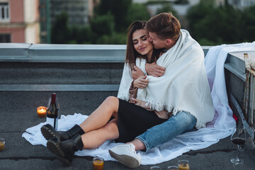 Wall Mural - Beautiful young loving couple on a surprise romantic date on a roof top. Picturesque view, skyscrapers on background. Wine, candles, kisses on holiday Saint Valentine's Day celebration outdoors