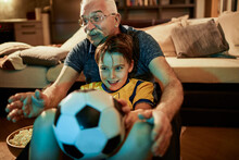 Young Boy Watching Football Game Soccer Match With Grandfather At Home