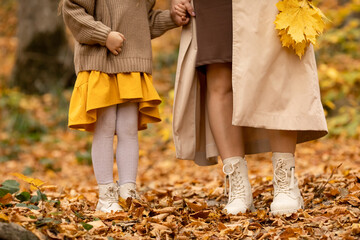 Wall Mural - Mom with child little girl walking in autumn park. Closeup of kid and mom legs in shoes walking through fall autumn leaves and foliage