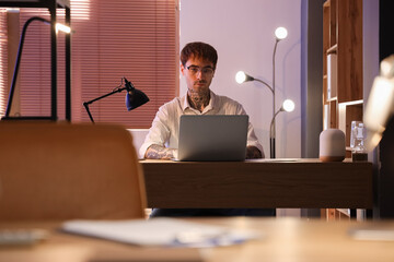 Wall Mural - Young tattooed man working with laptop in office at night