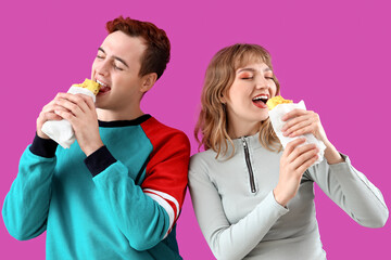 Sticker - Young couple eating tasty sandwich wraps on purple background