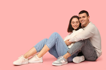 Sticker - Happy young couple sitting on floor and hugging against pink background