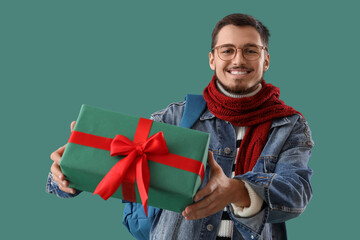 Canvas Print - Young man in winter clothes with Christmas gift on green background