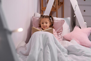 Wall Mural - Cute little girl reading story in bedroom at night