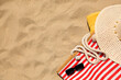 Striped beach bag, sunglasses, towel and hat on sand, flat lay. Space for text