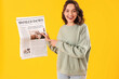 Young woman with newspaper on yellow background