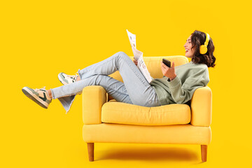 Poster - Young woman with newspaper and mobile phone in armchair on yellow background