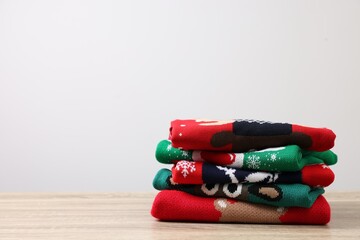 Sticker - Stack of different Christmas sweaters on wooden table against light background. Space for text