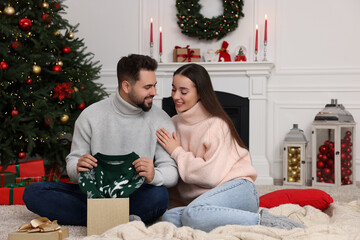 Wall Mural - Happy young man opening Christmas gift from his girlfriend at home