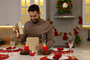 Sticker - Happy young man opening Christmas gift at table in kitchen