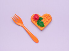 Orange Plastic Fork With A Cookie Figurine On A Purple Background.