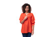 portrait of a bright young caucasian brunette woman with curly hair dressed in an orange shirt pointing her hand in surprise