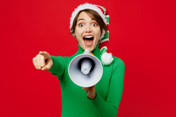 Wall Mural - Young woman wear green turtleneck Santa hat posing scream in megaphone announce sale Hurry up point finger camera on you isolated on plain red background Happy New Year 2024 Christmas holiday concept