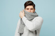 Young sad tired exhausted ill sick man in gray sweater cover mouth with scarf isolated on plain blue background studio portrait. Healthy lifestyle disease virus treatment cold season recovery concept.