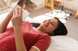 © Wavebreak Media - Happy biracial woman lying on bed and reading a book at home, copy space