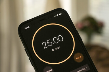 A phone with a black and orange 25-minute timer to study with the pomodoro method on a blurry background