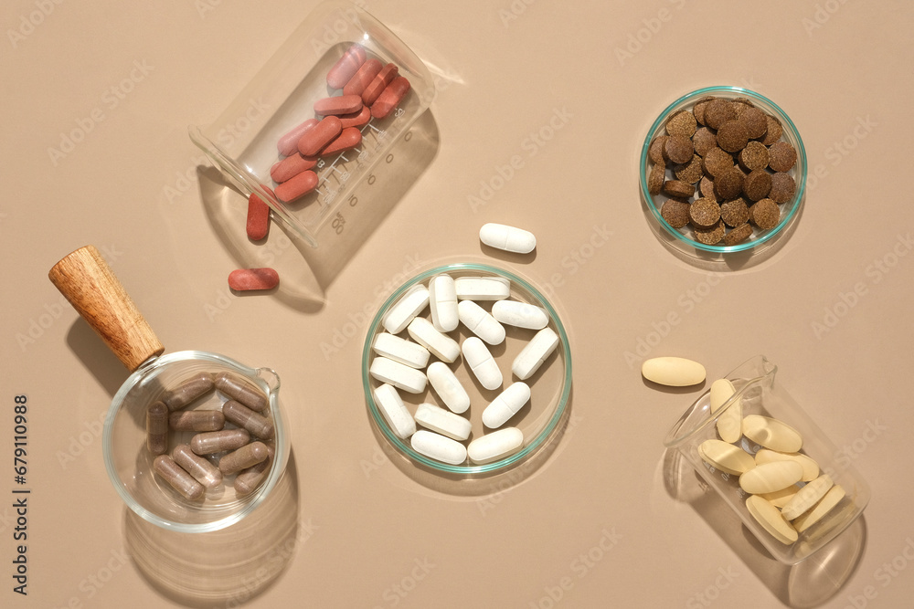 Pills of different colors are contained in glassware on a pastel ...