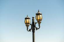 An Old Lamp Post With Two Lanterns And Aged Glass Darkened By Time, Against A Backdrop Of Blue Sky.