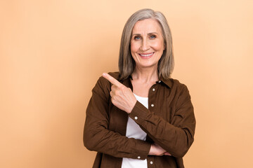 Poster - Photo of positive toothy beaming woman dressed brown shirt hand directing at offer empty space isolated on pastel color background