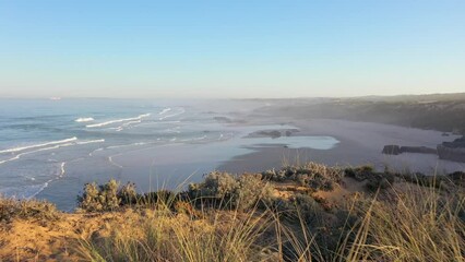 Canvas Print - Aerial view of Praia do Malhao beach at sunrise with fog and haze in Portugal. flying over a shore with dry grass and a rocky abyss