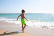 Cute little boy playing on the beach on summer holidays. Joyful child in nature with beautiful sea, sand and blue sky. Happy kid on vacations at seaside running in the water and having fun
