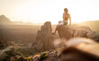 junge Wandererin sitzt auf einem großen Felsen und genießt den Sonnenuntergang