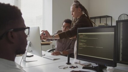Medium shot of multiracial couple of colleagues having discussion while working on computer presentation and their Black male colleague writing program code in foreground