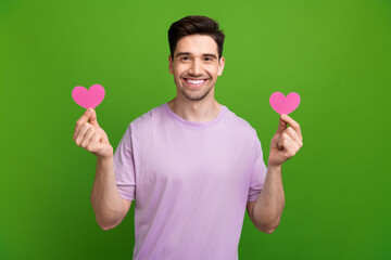 Poster - Portrait of pleasant cheerful person wear violet t-shirt fingers holding two paper pink heart postcard isolated on green color background