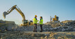 © Gorodenkoff - Back View Of Hispanic Female Project Manager And Caucasian Male Civil Engineer Discussing New Real Estate Project On Construction Site. Industrial Excavators Digging The Ground For Building Foundation