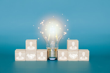 Teamwork concept, businessman icon on a wooden block and a glowing light bulb in the middle, teamwork allows ideas to evolve and help each other find solutions.