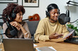 Young African American male radio presenter in headphones talking in microphone and looking at paper with text during interview with guest