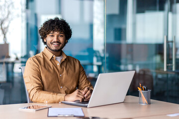 portrait of young successful businessman inside office at workplace, hispanic smiling and looking at